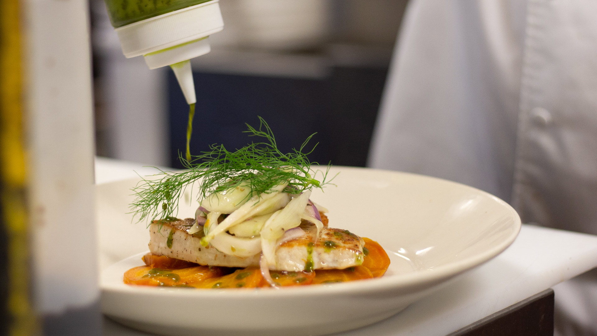 A chef finishing a plated fish dish at Cristof’s